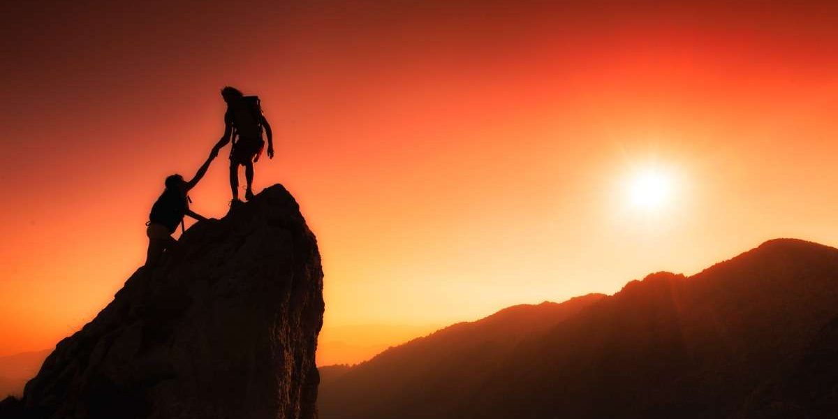 A strong leader, with a determined expression, pulls a person up a steep rock face. The person being pulled is reaching up to grasp the leader's outstretched hand.