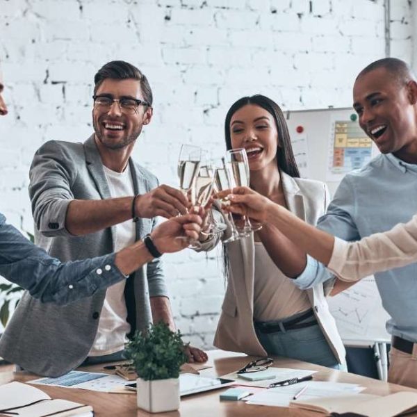 A group of diverse young professionals, standing in a modern board room, raise their glasses in a toast, celebrating a success.